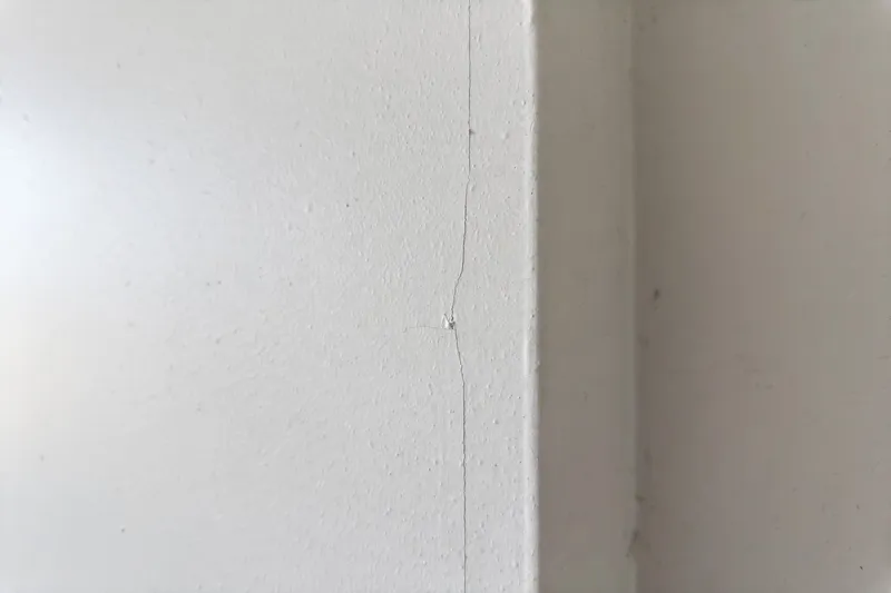Close-up of a thin hairline crack in a drywall wall near a corner (illustrative photo)